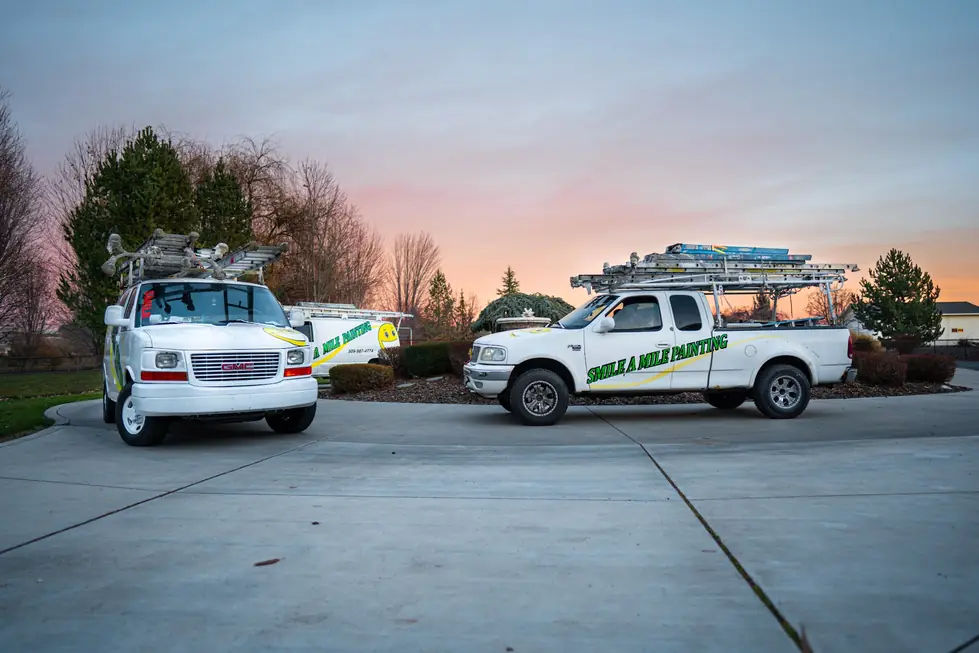 Two white Smile-A-Mile Painting work trucks with ladder racks at dusk