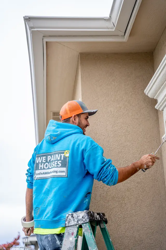 Smile-A-Mile painter brushing an interior wall corner from a stepladder